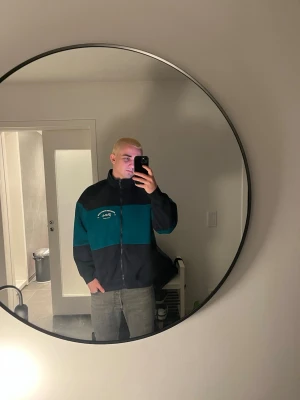 Stronger zip up - Säljer en snygg vindjacka från Peak Performance i mörkblått och turkost. Jackan har hög krage, dragkedja framtill och logga på bröstet. Perfekt för dig som vill ha en sportig och stilren look.