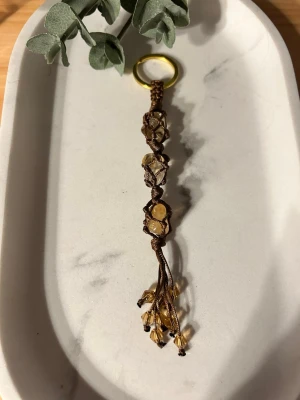 Handgjord Nyckelring/Väsksmycke med Citrin (trumlad) - Unik handgjord nyckelring med mörkbrun tråd och 3st små Citrin (trumlad ) sten/kristall. Ring i rostfritt stål guldfärgad, nertill glaspärlor  i änden. Perfekt som accessoar till väskan eller nycklarna.