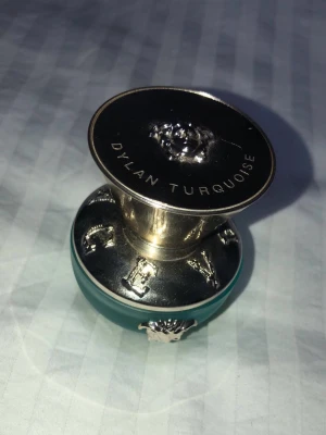 Versace Dylan Turquoise parfym - Säljer en Versace Dylan Turquoise parfym i en snygg turkos glasflaska med silverfärgade detaljer och Versaces ikoniska Medusa-huvud. Flaskan har en rund, lyxig form och metallock med text. Perfekt för dig som gillar exklusiva dofter och stilren design.