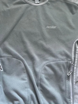 Palace X Adidas fleece  - Mjuk och stilren grå fleece tröja från Palace skateboards collab med Adidas. diskret broderad logga på bröstet. Tröjan har två stora fickor med dragkedja och vita detaljer längs kanterna. Perfekt för lager-på-lager och streetwear. Den vart slutsåld direkt, hade helt glömt att jag hade den och vill se om nån är intresserad ut av den! Väldigt rare piece och super bra skick för att vara så pass gammal modell, mvh hittade inte den förens nu :,)
