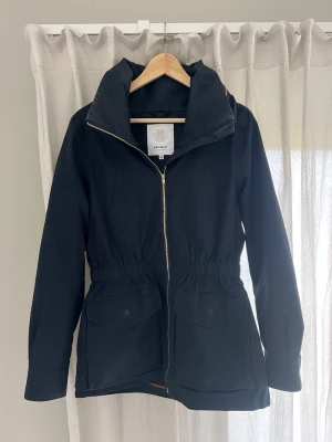 Jacka Elvine - Mörkblå med gulddetaljer. Dold luva. 