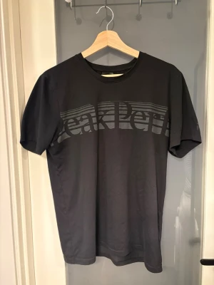 Svart Peak Performance t-shirt - Snygg svart t-shirt från Peak Performance med stort tryck över bröstet. Klassisk passform och rund halsringning. Perfekt till jeans eller shorts för en clean och enkel look.