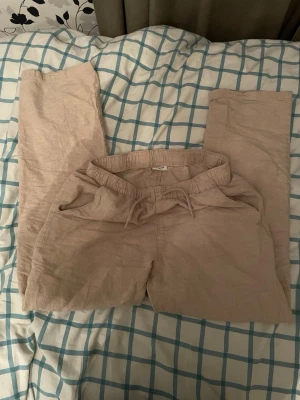 Beiga linnebyxor från Kappahl - Säljer ett par beiga linnebyxor från Kappahl med avslappnad passform och resår i midjan samt dragsko. Byxorna har raka ben och är tillverkade i ett luftigt linnematerial som passar perfekt för en chill och stilren look.