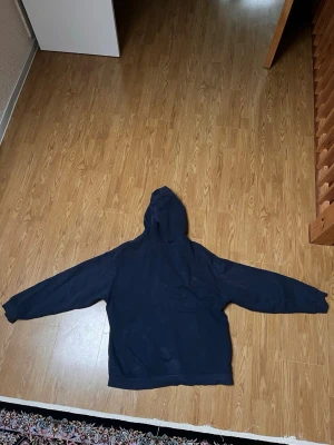 Mörkblå zip hoodie med huva - En enkel och stilren mörkblå hoodie med dragkedja framtill och stor huva. Hoodien har långa ärmar och ribbade muddar vid ärmslut och nederkant. Tillverkad i mjukt bomullsliknande material som känns skönt mot huden. Perfekt för en avslappnad look. Den har några vita fläckar vet ej vart de har kommit ifrån 