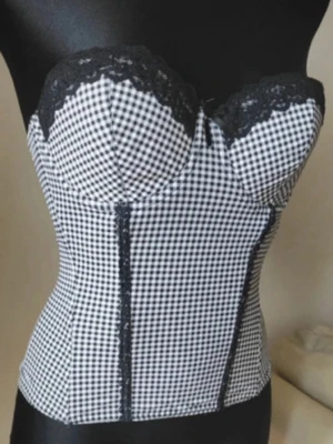 Rutig svartvit korsett med spets - Supersnygg korsett i svartvitt rutigt mönster med svarta spetsdetaljer upptill. Figurnära passform och markerade sömmar framtill ger en riktigt trendig siluett. Perfekt att styla med jeans eller kjol för en edgy look. Passar mellan Xs till M