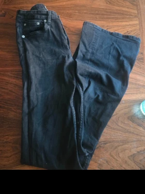 Svarta utsvängda jeans - Säljer ett par svarta jeans med utsvängda ben och klassisk femficksmodell. Jeansen har hög midja och raka sömmar, perfekta för en trendig och avslappnad stil. Materialet är denim i bomull och de har knapp- och dragkedjestängning.