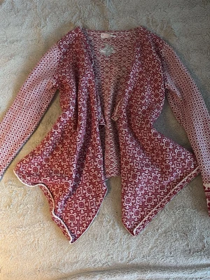 Rödvit mönstrad kofta Odd Molly - Säljer en röd och vit stickad kofta från Odd Molly med snyggt geometriskt mönster. Koftan har öppen front och långa ärmar, samt broderad logga på ryggen. Perfekt för dig som gillar unik design och sköna material.