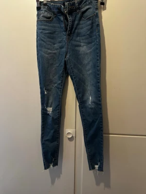 Blå skinny jeans från Even&Odd - Säljer ett par blå skinny jeans från Even&Odd med slitna detaljer och råa benslut. Jeansen har klassisk femficksmodell och är tillverkade i stretchigt denimtyg för en bekväm passform. Perfekta för en avslappnad och trendig look.