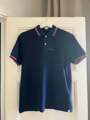 Prada piké navy – size S - Prada piké i navy med diskret logo framtill.  Storlek: S Skick: Bra skick, inga tydliga defekter  Klassisk modell med fina detaljer vid krage och ärmar. Perfekt för en clean och stilren look.  Skriv vid frågor eller för fler bilder