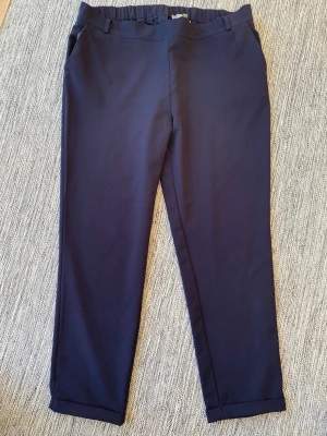 Mörkblå kostymbyxor med raka ben - Eleganta mörkblå byxor med resår i midjan och praktiska fickor. Byxorna har en avslappnad passform och en stilren design som passar både till vardags och till mer formella tillfällen.  Finns en liten tråd på rumpan i övrigt i bra begagnat skick   Mått Midjan: ca 49 cm Längd från grenen och ner: ca 75 cm  94% polyester och 6% elastan  Kommer från ett djur och rökfritt hem