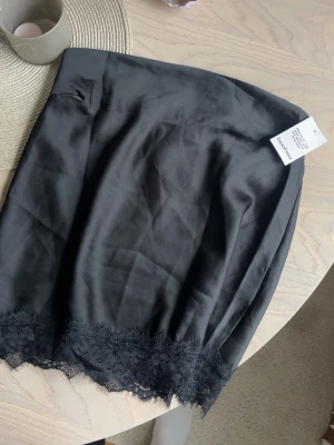 Satintopp - Snygg svart satintopp från Boohoo med dekorativ spetskant längst ner. Toppen har en enkel, rak passform och är gjord i ett mjukt, glansigt material som ger en elegant känsla. Helt ny säljer då den var för stor för mig