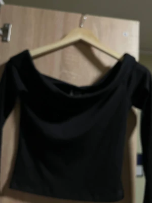 Svart offshoulder topp från H&M - Säljer en svart, ribbad offshoulder topp från H&M i storlek S. Toppen har lång ärm och en snygg croppad passform som passar perfekt till jeans eller kjol. Materialet är mjukt och stretchigt för en bekväm känsla. Använt 1 gång 