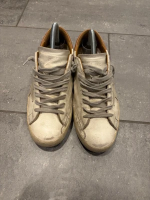 Golden Goose Superstar sneakers beige - Snygga Golden Goose Superstar sneakers i beige läder med grå mockadetaljer och grå snörning. Skorna har en brun hälkappa och den ikoniska stjärnan på sidan. Perfekta för en avslappnad och trendig stil. Finns påse också, glömde att ta bild.