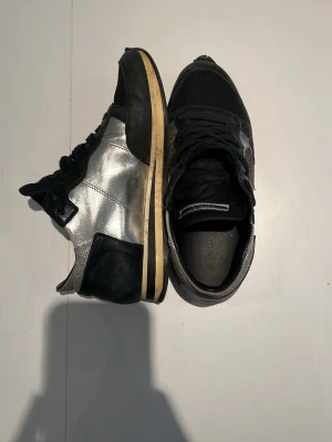 Philippe Model svarta/silver sneakers - Snygga sneakers från Philippe Model i svart och silver. Ovandelen är i en mix av mesh och läder med metallicdetaljer. Klassisk låg modell med svart snörning och beige sula. Perfekta för dig som vill ha en unik touch på din outfit. Inge box eller og medföljder. Lite små i storleken skriv vid frågor.