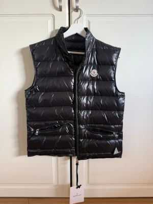 Moncler Gui Down Väst - Säljer min Moncler “Gui-väst” i storlek 1. Västen är helt oanvänd och har fortfarande prislappen kvar. Perfekt som lätt ytterplagg nu inför våren.  Storlek 1 med normal passform. Hör gärna av dig vid frågor eller om du vill ha fler bilder 🙂 