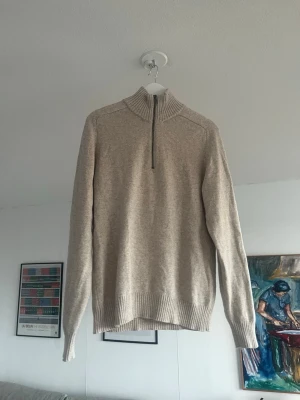 Beige stickad tröja med halvzip - Snygg beige stickad tröja med halvzip och hög krage. Tröjan har långa ärmar och ribbade muddar vid ärmslut och nederkant. Perfekt för lager på lager och enkel att matcha med olika outfits. Tröjans storlek är S men sitter som en M.