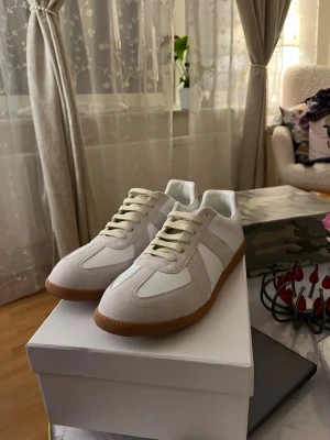 Maison margiela skor - Snygga sneakers i vitt och beige från maison margiela. Använda ungefär 1-2 gånger men de är tyvärr för stora för mig då jag fick de i present. De är i storlek 41 men hyfsat stora i storleken. Kommer även i orginal låda.                                          Kan gå ner i pris om de är snabbaffär.         