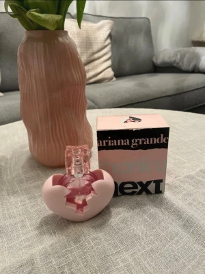Ariana Grande Thank U Next parfym - Säljer en Ariana Grande Thank U Next parfym med en unik hjärtformad flaska i ljusrosa plast och transparent rosa glas. Parfymen kommer med originalkartong och har en modern, ungdomlig design som sticker ut på hyllan.