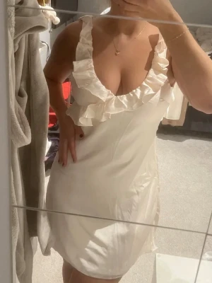 Satin klänning - Kort satinklänning med öppen rygg och volanger. Typ krämvit/lite rosa aktig i färgen. Hade som studentklänning. Nypris 1500