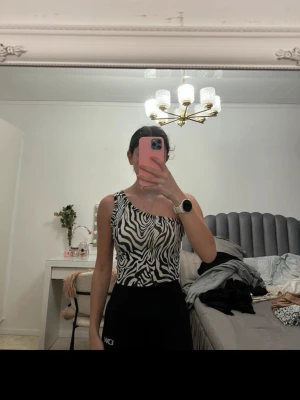 Zebramönstrad ärmlös topp - Säljer en snygg zebramönstrad topp i svart och vitt. Toppen är ärmlös med breda axelband och har en tight passform som framhäver figuren. Perfekt att styla med höga byxor eller kjol för en trendig look.