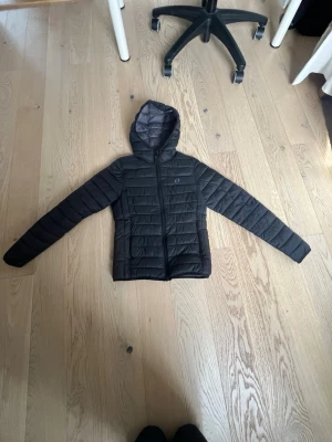 Svart pufferjacka från Hangten XS - Snygg svart dunjacka från Hangten med huva och quiltad design. Jackan har ett litet hål på ena sidan av dragkedjan men syns nästan inte. Priset kan alltid diskuteras💕