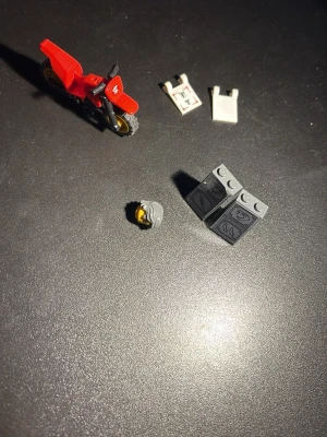 LEGO motorcykel och minifigurdela - Säljer en röd LEGO motorcykel med gulddetaljer samt flera minifigurdela, inklusive två vita överkroppar, ett grått hår och två svarta block med tryck. Perfekt för dig som gillar att bygga och mixa egna LEGO-figurer.