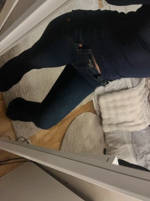 True religion lågmidjade mörkblå jeans - Snygga mörkblå jeans med klassisk bootcut-passform. Jeansen har en figurnära siluett upptill och utsvängda ben nertill. Tillverkade i mjukt denimtyg med diskreta slitningar och kontrastsömmar. Perfekta för en trendig och avslappnad look. Byxorna är i längd 32 men har sytt upp dom lite, men det skulle inte vara några problem få dom som vanliga igen om man spretar upp ändarna igen.