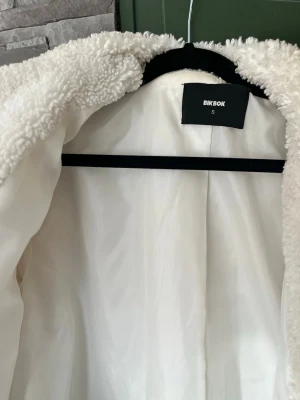 Vit teddyjacka från Bik Bok - Säljer en fluffig och oversized vit teddyjacka från Bik Bok. Jackan har bred krage, dolda knappar framtill och två sidofickor.