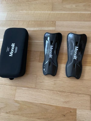 Monolit benskydd i kolfiber - Säljer ett par svarta benskydd från Monolit i kolfiber med ergonomisk form och lätt vikt. De har en blank finish och kommer med ett svart skyddsfodral. Perfekta för dig som vill ha smidiga och tåliga benskydd till fotbollen.