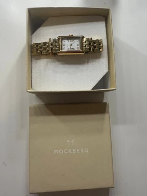 Guldfärgad klocka Mockberg - Klocka från Mockberg, knappt använd men har förkortat armbandet. Bitarna finns kvar och skickar med dem vid köp, så är det bara att gå till t.ex guldfynd och anpassa armbandet efter din egen storlek! 🥰🥰