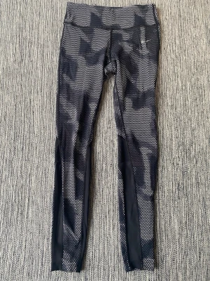 Svarta mönstrade leggings från Nike strl S - Nike Dri-FIT löpartights för kvinnor i storlek S. Tillverkade i material som transporterar bort fukt för att hålla användaren torr under löpning. Tightsen har ett svart mönster med reflexdetaljer för ökad synlighet. Designade för att ge komfort och rörelsefrihet vid sportaktiviteter. Finns en liten ficka med dragkedja baktill  Sparsamt använda och i fint begagnat skick   Mått Midjan: ca 34 cm Längd från grenen och ner: ca 72 cm  Polyester och elastan   Kommer från ett djur och rökfritt hem