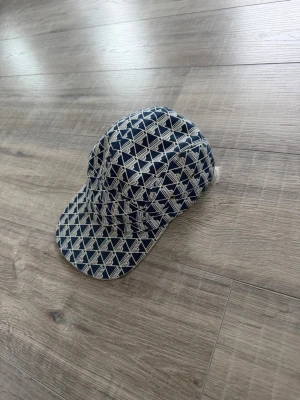Fin och stilig Lacoste keps - Snygg keps i blått och vitt med grafiskt mönster över hela ytan. Klassisk form med böjd skärm och metallöljetter på sidan för ventilation. Tillverkad i ett mjukt tygmaterial som känns bekvämt på huvudet. 