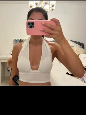 Vit halterneck croppad topp - Säljer en vit croppad halterneck topp med knyt i nacken. Toppen har djup urringning och är ärmlös, perfekt för varma dagar eller sommarens outfits. Materialet känns mjukt och stretchigt, troligen bomull eller polyester.