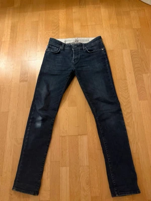 Tramarossa jeans - Säljer ett par mörkblå jeans med rak passform och klassisk femficksdesign. Jeansen har en snygg tvätt och kan vikas upp nertill för en trendig look. Perfekta till vardagsstilen och tillverkade i mjukt denimtyg. Fickan inne i högerfickan har släppt lite men annars e de bra