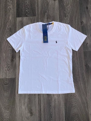 Vit t-shirt från Polo Ralph Lauren - Klassisk vit t-shirt från Polo Ralph Lauren med rund halsringning och korta ärmar. T-shirten har den ikoniska lilla logotypen broderad på bröstet. Tillverkad i mjuk bomull för en skön och stilren look.