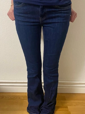 Mörkblå bootcut jeans - Snygga mörkblå bootcut jeans med klassisk femficksmodell och normal midja. Jeansen har en lätt utsvängd passform nedtill och är tillverkade i ett mjukt denimtyg. Köpte dessa SJUKT snygga jeans från Nelly, men märket Gina tricot. Älskar dem verkligen och ska definitivt köpa dem igen, dock en storlek större för de passade inte mina höft. Dem är använda men bara ett fåtal gånger, min lilla syster tog på sig dem en gång vilket ni kan se vid ena benet. För fler bilder fråga!