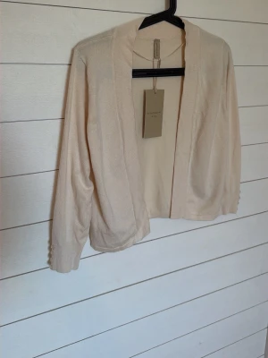Beige kofta från MyEssential Wardrobe - Helt ny: Snygg beige kofta från MyEssential Wardrobe med öppen front och långa ärmar. Enkel och stilren design som passar perfekt till lager-på-lager-look. Mjukt och tunt material som känns skönt mot huden. Perfekt för vår och sommar.Mindre defekt se bild 7. 