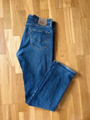 Blå raka jeans från Levi's - Klassiska blå jeans från Levi's med raka ben och femficksmodell. Jeansen har en mörkblå tvätt, tydliga bakfickor med V-formad söm och röd Levi's-tag. Tillverkade i bomullsdenim med en tidlös look som funkar till allt.