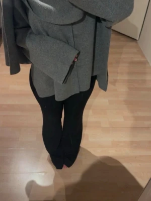 Zara Cape Jacka Poncho - Säljer en grå oversized kappa med bred krage och vida ärmar. Kappan har en rak passform och är tillverkad i ett tjockare tyg som ger en stilren look. Perfekt för dig som gillar minimalistisk och modern stil.