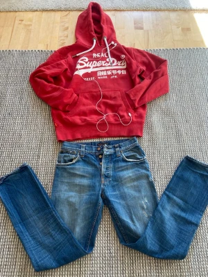 Blå Nudie jeans - Säljer ett par klassiska blå jeans från Nudie med knäppning fram och slitningar på benen. Jeansen har fem fickor och en snygg tvätt med ljusa detaljer. Perfekt för dig som gillar en avslappnad och trendig look. W29 L32