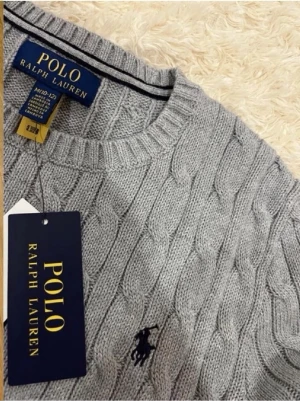 Grå kabelstickad tröja Polo Ralph Lauren - Säljer en snygg grå kabelstickad tröja från Polo Ralph Lauren. Tröjan har rund halsringning, ribbade muddar och den klassiska broderade loggan på bröstet. Perfekt för dig som gillar stilrena och tidlösa plagg i mjukt material.