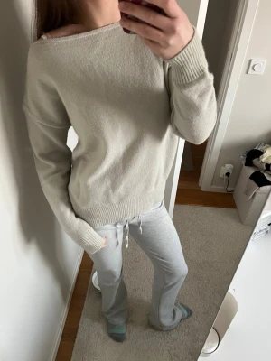 Beige stickad tröja med bred hals - Grå stickad  off-shoulder tröja. Tröjan har långa ärmar och ribbade muddar vid ärmslut och nederkant. Enkel och stilren design som är lätt att matcha med olika stilar.