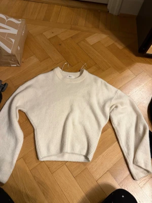 Vit stickad tröja Gina Tricot - Mysig vit stickad tröja från Gina Tricot i ullblandning. Tröjan har rund halsringning, långa ärmar och bred ribbstickad kant nedtill. Perfekt för kalla dagar och enkel att matcha med olika outfits.