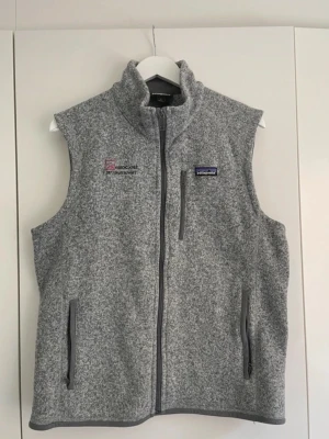 Grå fleeceväst från Patagonia - Patagonia väst med ‘TA Associates 2017 sales summit’ broderat på bröstet. Storlek L, men liten i storleken. Använder vanligtvis M. Se mått på bilder. Bra skick.  Bröstvidd 52cm Längd 64cm   