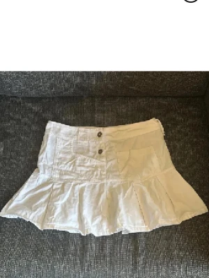 Vit volangkjol med fickor - Snygg vit kortkjol med volangkant och två stora fickor framtill. Kjolen har knappar i midjan och är tillverkad i ett lätt bomullstyg, perfekt för varmare dagar. Enkel och stilren design som passar till många olika looks. Stretchig💕