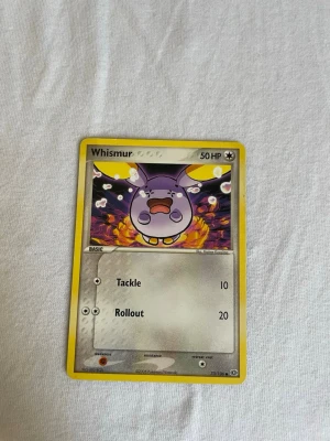 Pokémonkort Whismur 73/106 - Säljer ett original Pokémonkort med Whismur från serien EX Emerald, nummer 73/106. Kortet har gul ram, färgglad illustration och är tryckt på klassiskt glansigt pappmaterial. Perfekt för samlare eller Pokémonfans!