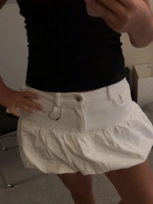 Vit volangkjol/jeanskjol - Snygg vit kortkjol med volang. Kjolen har bälteshällor och knappstängning framtill. Perfekt för en trendig och fräsch look.