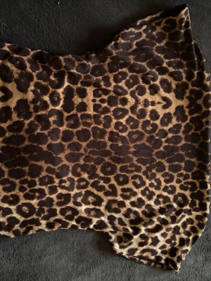 Leopardmönstrad kortärmad topp med urringad rygg - Säljer en cool kortärmad topp som är en magtröja med leopardmönster i bruna och beige toner. Toppen har en klassisk urringad rygg detalj och är tillverkad i ett mjukt och stretchigt material som känns skönt mot huden. Perfekt för dig som vill sticka ut med ett djurinspirerat print.