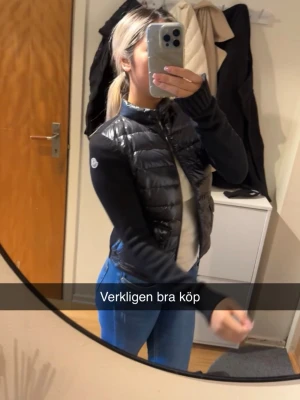 Svart cardigan från Moncler - Snygg svart cardigan från Moncler med quiltad front och två fickor med lock. Västen har stickade ärmar och hög krage, perfekt för lager-på-lager. Materialet är glansigt och ger en cool look. Storlek xs passa mig som även bruka ha s. Använt några få gånger men är i toppen skick!!