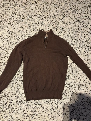 Brun stickad tröja med halvzip - Snygg brun stickad tröja från John Henric med halvzip och hög krage. Tröjan har ribbade muddar vid ärmslut och nederkant samt en mjuk känsla. Perfekt för lager-på-lager och passar till många olika stilar.